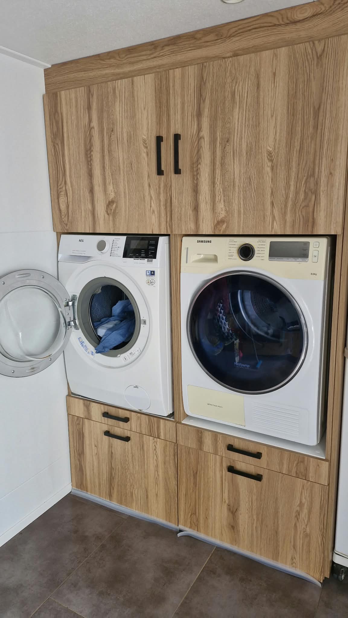 Na: houten kastenwand met wasmachine en droger op verhoogde plek