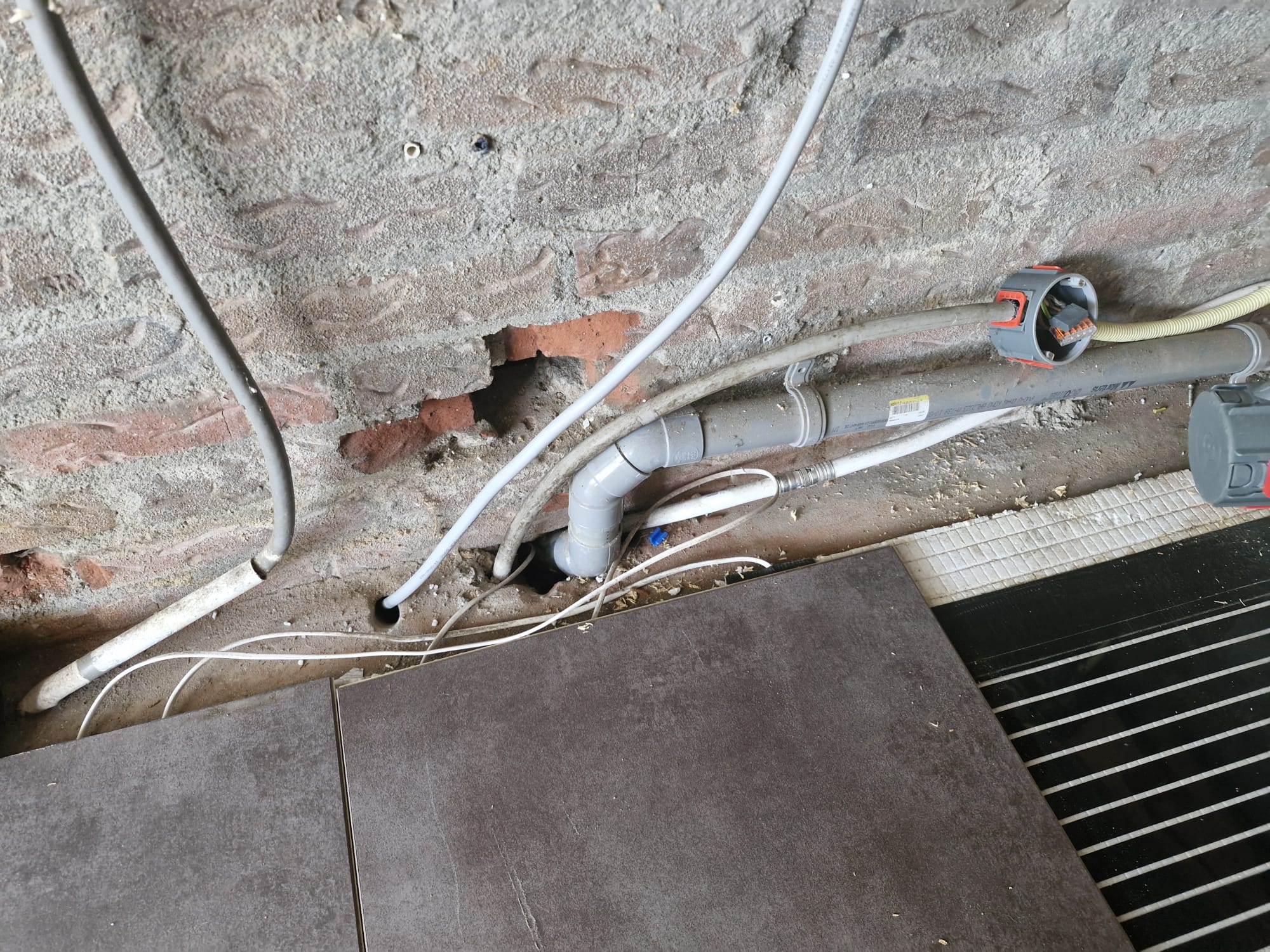 Afvoer-, water- en elektraleidingen langs de muur met vloerverwarming