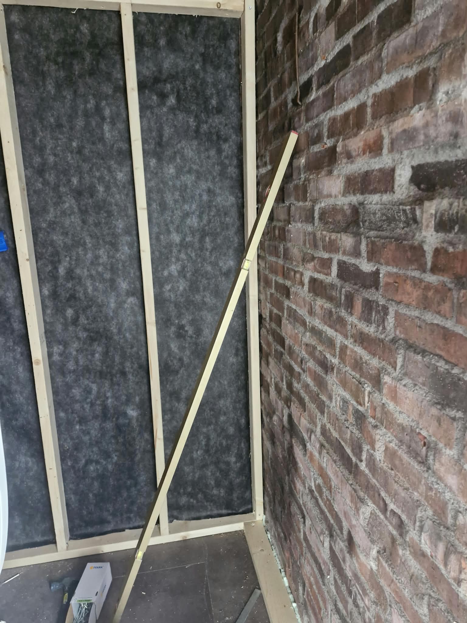 Houten wandframe met zwarte dampremmende folie naast de bakstenen muur